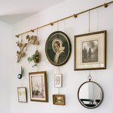 Wall with various framed pictures and a round mirror, featuring a decorative gold rod.