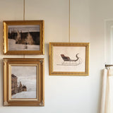 Three gold-framed pictures on a wall with a white background